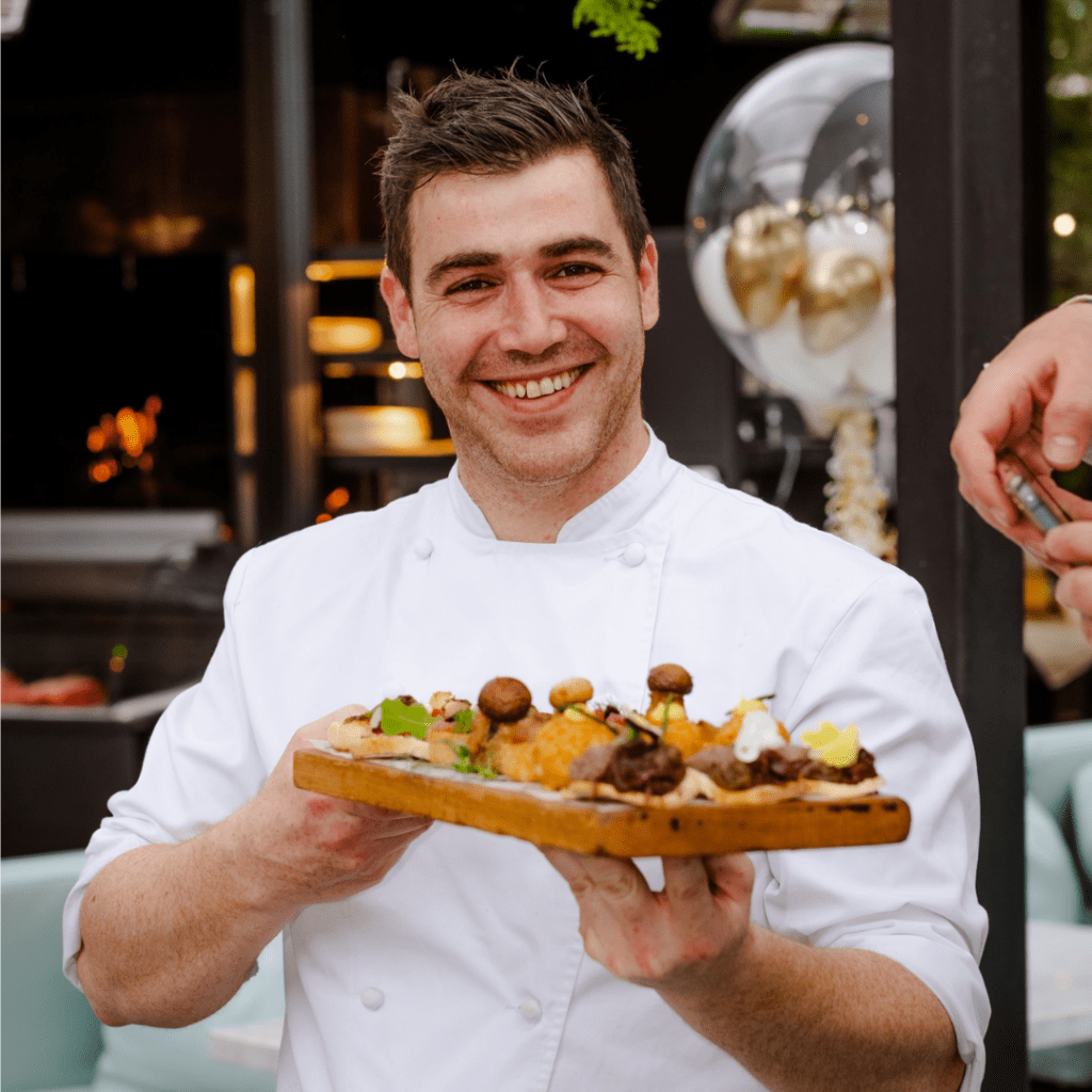 Chef is holding entrées on a wooden tray.