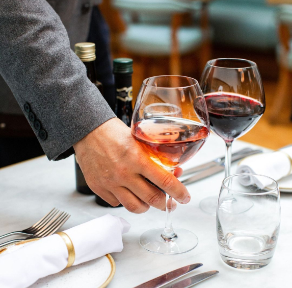 A person is picking up a glass of wine from a table.